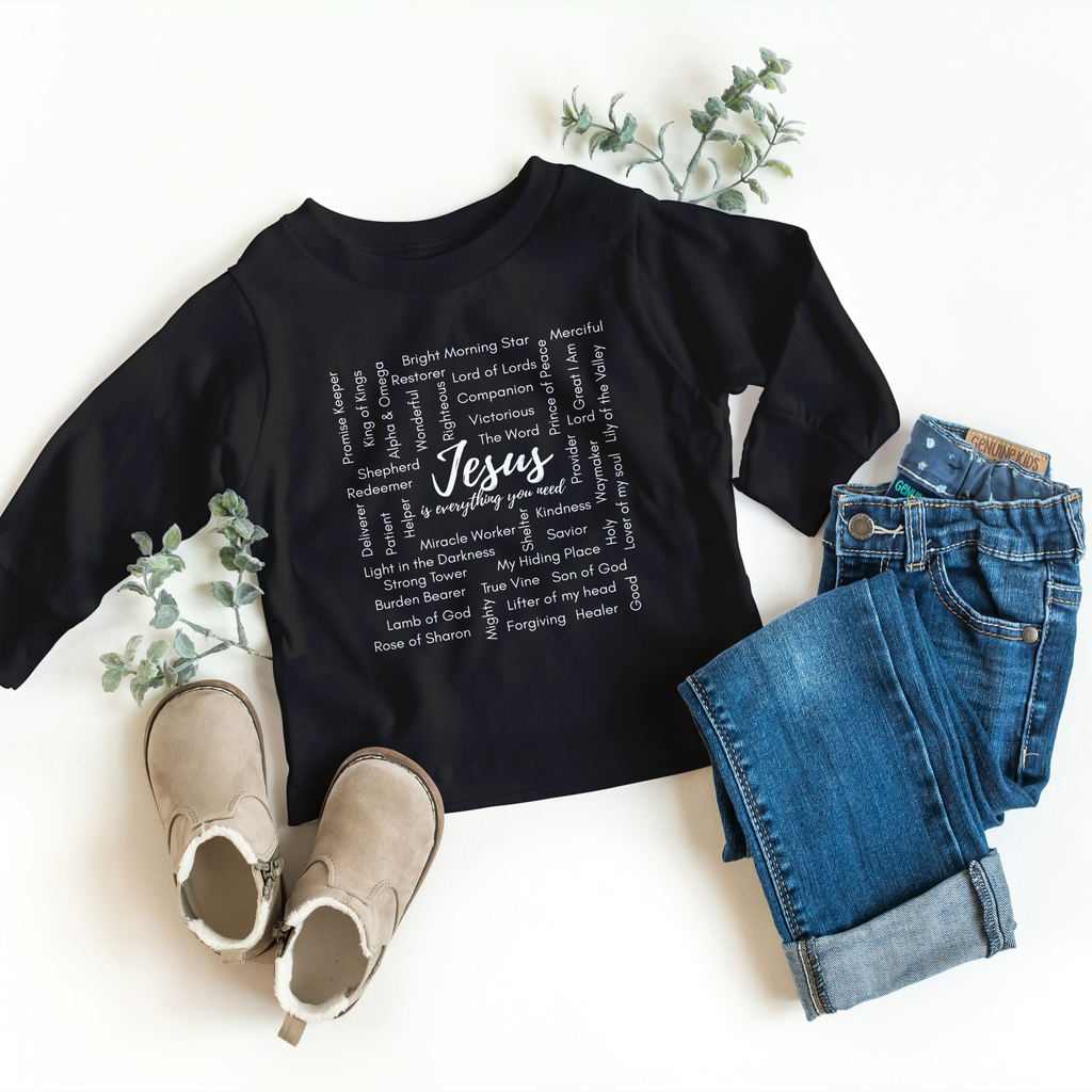 Black t-shirt with 'Jesus' text, paired with jeans and shoes on a white background