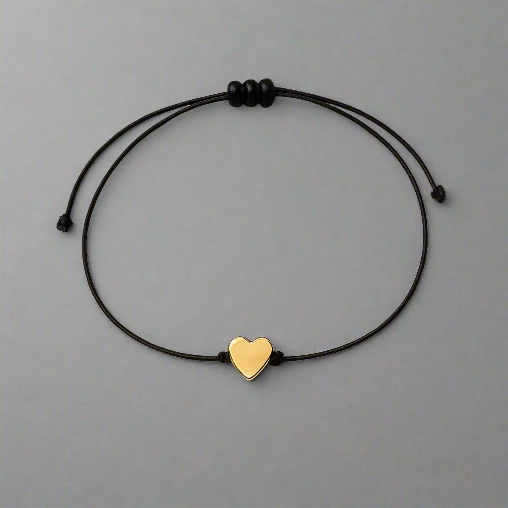 Black cord bracelet with a gold heart charm on a gray background