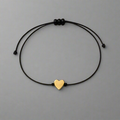 Black cord bracelet with a gold heart charm on a gray background